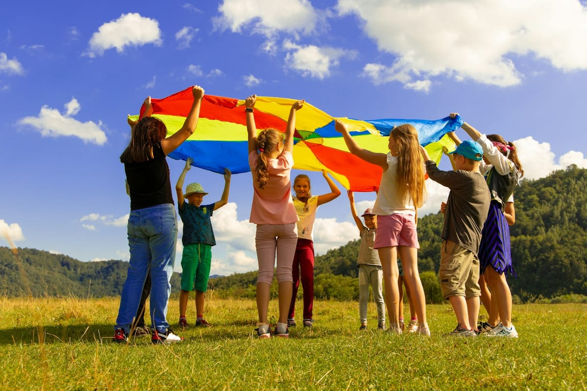 Children playing with a rainbow parachute on a hillside