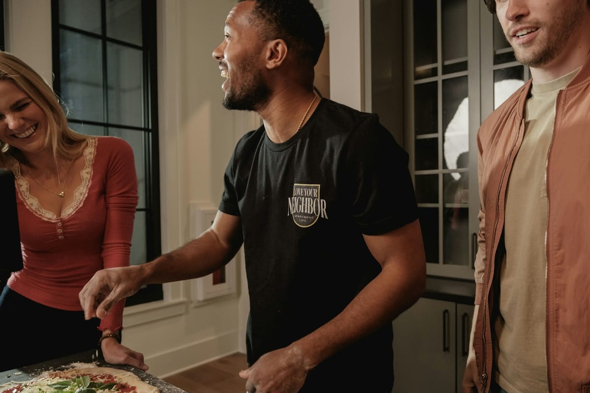 Friends laughing while making pizza together in a kitchen